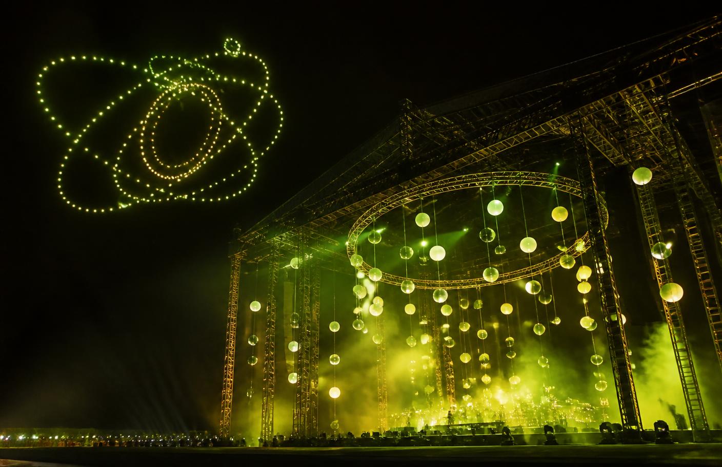 Kinetic light spheres suspended over a stage with a drone light formation overhead